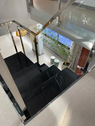 Escada revestida em mármore preto com guarda-corpo de vidro