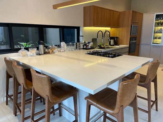 Cozinha ampla com ilha em pedra clara e bancada de apoio