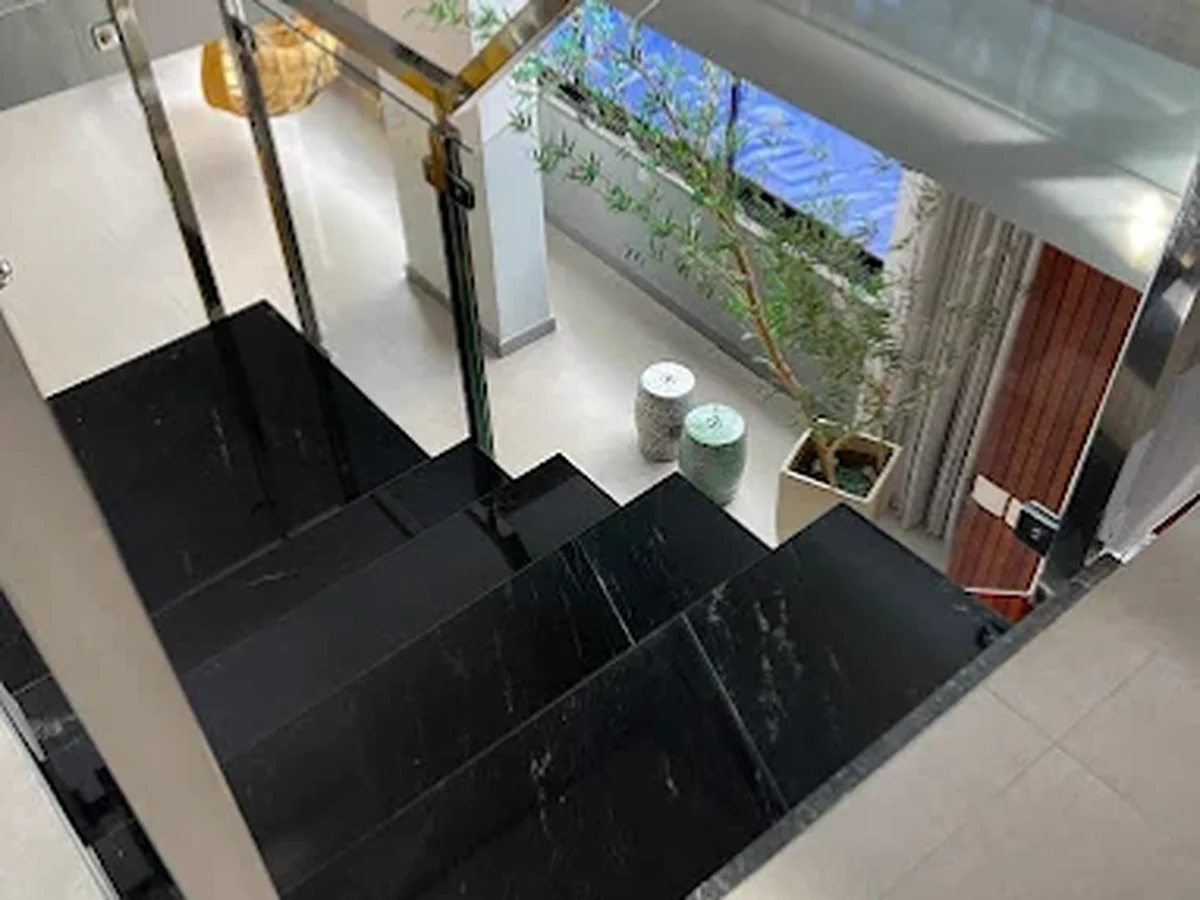 Escada revestida em mármore preto com guarda-corpo de vidro